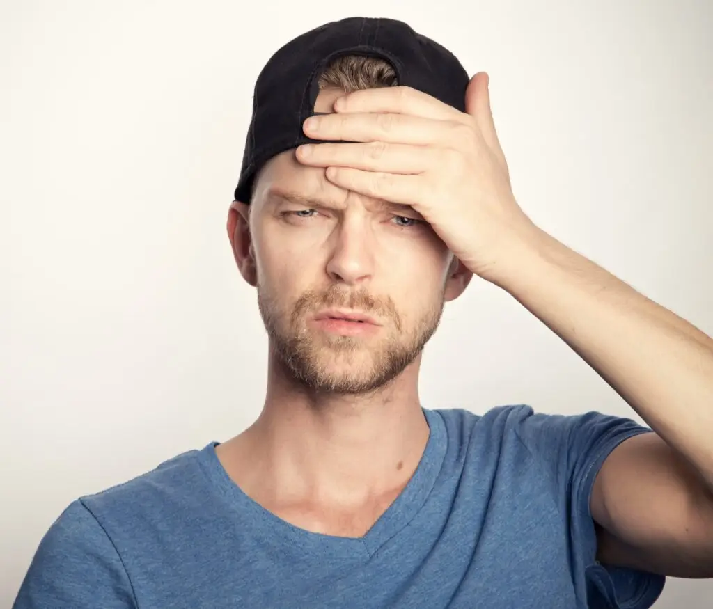 Man in a black cap holding his forehead.