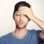 Man in a black cap holding his forehead.